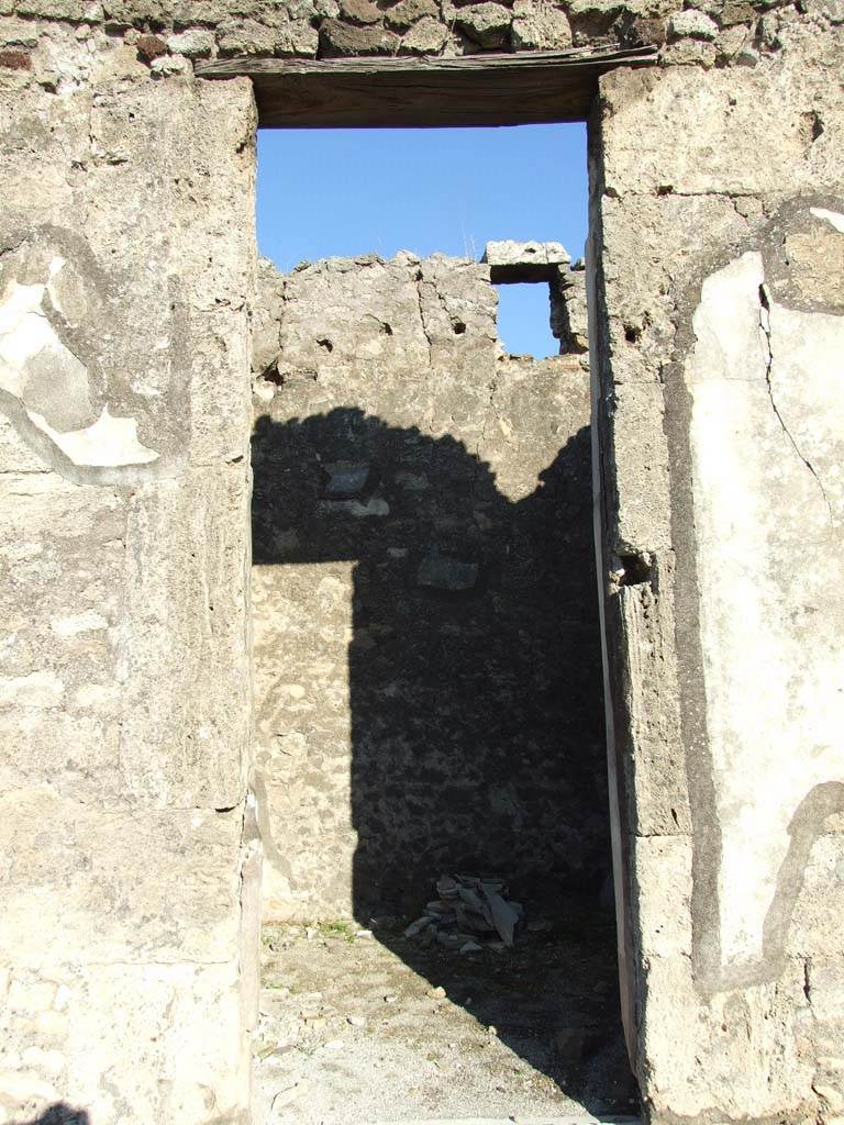 VII.15.2 Pompeii. December 2007. Doorway to cubiculum in centre of east side of atrium.
In the panel on the left of the doorway would have been the painting of Spring.
According to Sogliano –
“Spring, in the shape of a woman flying in the air, turning to the right, wearing a green robe and red mantle, which covered her left arm and lower body; she held with her left hand the four legs of a lamb, which she carried on her shoulder, and in the right hand a wicker-basket with some milk/ricotta.” 
(La Primavera, personificata in una donna liberata in ara, volta verso destra, con veste verde e manto rosso, che le covre il braccio sinistra e la parte inferiore del corpo; tiene con la sinistra le quattro zampe di un agnello, che porta sul collo, e nella destra un meta di latte nella sua fiscella.)
(Bull.Inst. 1872, p.166) (Fiorelli, Scav. d. Pomp. p.129 n. 270. Descr. Pomp, (p.305)
See Sogliano, A., 1879. Le pitture murali campane scoverte negli anni 1867-79. Napoli: Giannini, (p.76, no. 459)
In the panel on the right of the doorway would have been the painting of Winter.
According to Sogliano –
“Winter, in the shape of a woman flying in the air and turning to the left, with a dark-yellow robe, fluttering green mantle, which also covered her head, and yellow shoes; she held in the right hand, a branch devoid of leaves, and in the left lowered hand, Gaedechens saw two ducks of various colours, now vanished.”
(L’Inverno in figura do donna liberata in aria e volta a sinistra, con chitone giallo-scuro, manto verde svolazzante, che le covre anche la testa, e calzari gialli; tiene nella destra appoggiato all’omero corrispondente un ramo privo di foglie, e nella sinistra abbassata [Rudolf] Gaedechens vide due anitre vario pinte, ora svanite.)
(Bull.Inst. 1872, p.166) Fiorelli, Scav. d. Pomp, (p.130, n.281): Desc. Pomp, (p.198).
See Sogliano, A., 1879. Le pitture murali campane scoverte negli anni 1867-79. Napoli: Giannini, p.77, no.464)
