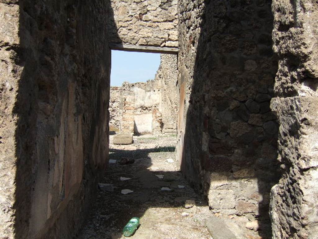VII.15.3 Pompeii. September 2005. Looking north along entrance corridor to atrium.
Embedded into the cocciopesto flooring were tiles/slabs of marble leading to the atrium. The zoccolo/dado/plinth of the walls was divided into panels imitating large marble slabs, whose veins were obtained with large white and black strokes.
The middle zone of the walls was simply painted in white. The doorway on the right leads to the latrine.