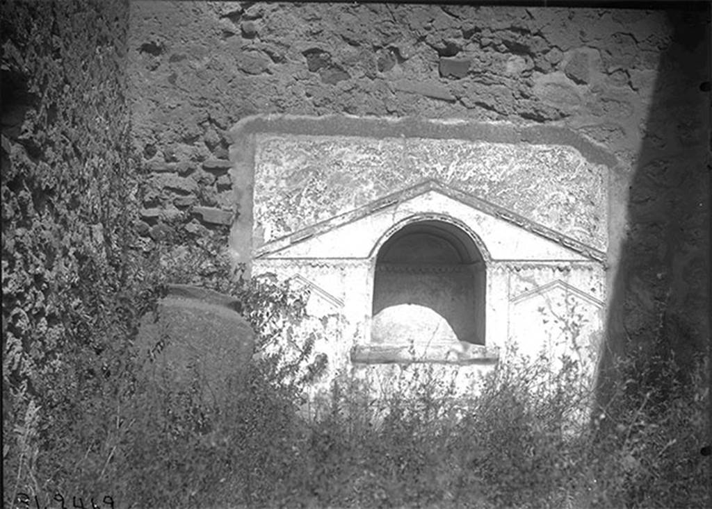 VII.15.8 Pompeii, 1931. Looking towards niche in north wall of garden area.
DAIR 31.2462. Photo © Deutsches Archäologisches Institut, Abteilung Rom, Arkiv.
According to Boyce, in the centre of the north wall of the garden area near the floor, was an arched niche.
The wall around it was covered with a rectangular panel of white stucco.
On this was an aedicula façade which was marked off with yellow and violet lines in low relief.
The work was delicately executed but somewhat irregular.
See Boyce G. K., 1937. Corpus of the Lararia of Pompeii. Rome: MAAR 14. (p.72, no.332, Pl.6,2)