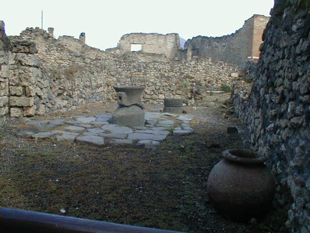 VII.16.6 Pompeii. September 2004. Looking north across workshop, at the rear was a doorway into VII.16.9. According to Eschebach, the doorway on the left would have led into a small room under the steps at VII.16.5.
At the rear on the left would have been a stairs to the upper mezzanine, with a latrine beneath. In the workshop were two dolia, three mortars, and two or three mills.
See Eschebach, L., 1993. Gebäudeverzeichnis und Stadtplan der antiken Stadt Pompeji. Köln: Böhlau. (p.347)