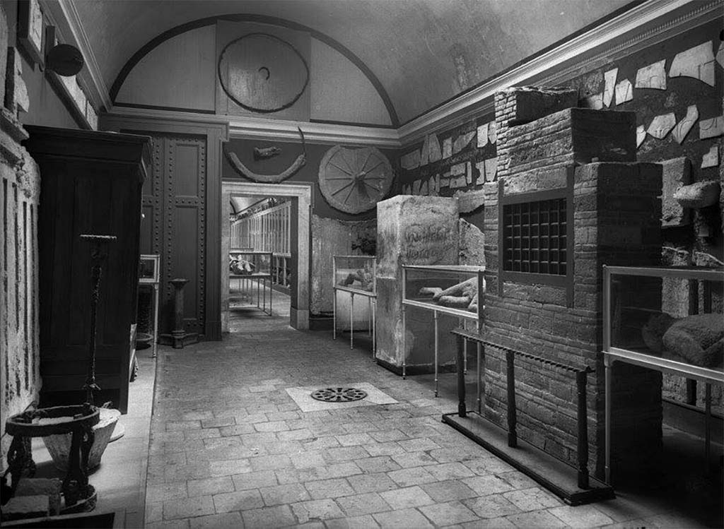 VIII.1.4 Pompeii Antiquarium. Old pre-1943 undated photo showing some of the contents of the antiquarium listed by Fiorelli in his guide.
Left of the doorway is the reconstructed door, right is the cast of an ancient door with locks and left the reconstructed cupboard, all drawn by Gusman (see below).
Photo courtesy Dr Sophie Hay.