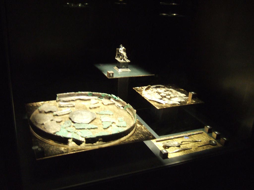 Silver found 20th September 1887 in VIII.2.23. Now in Naples Archaeological Museum.
Statuette of Giove seated on a throne (rear). Inventory number 116356.
Centre left is the remains of a silver tray. Inventory number 116363.
Centre right is the remains of a silver plate. Inventory number s.n.
Bottom right is a group of four silver items.
See Guzzo, P. (A cura di), 2006. Argenti a Pompei. Milano, Electa. (p. 134).