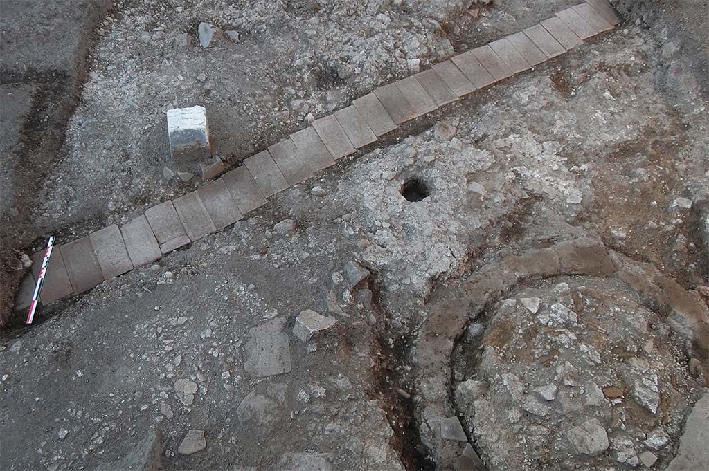 Fig. 17 – Pompéi, boulangerie VIII 4, 26-27 – Moitié méridionale de la salle des meules.
L’alignement de briques correspond au passage d’un câble électrique ; au sud-est de la salle, la fosse septique avant le début du dégagement de son remplissage.
Pris du sud. Cliché : S. Zanella /EFR.