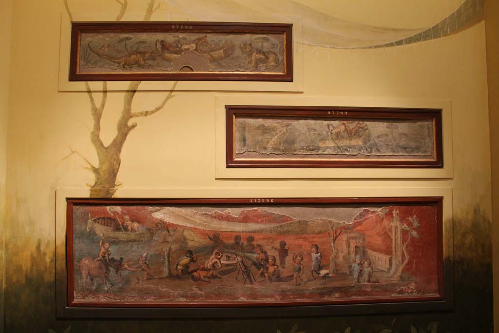 VIII.5.24 Pompeii. March 2014. Display of painting on a wall in Naples Archaeological Museum.
The lowest painting is a Nile banquet scene with pygmies. From a low wall connecting peristyle columns in VIII.5.24.
The upper paintings are from VII.2.25.
Foto Annette Haug, ERC Grant 681269 DÉCOR.
