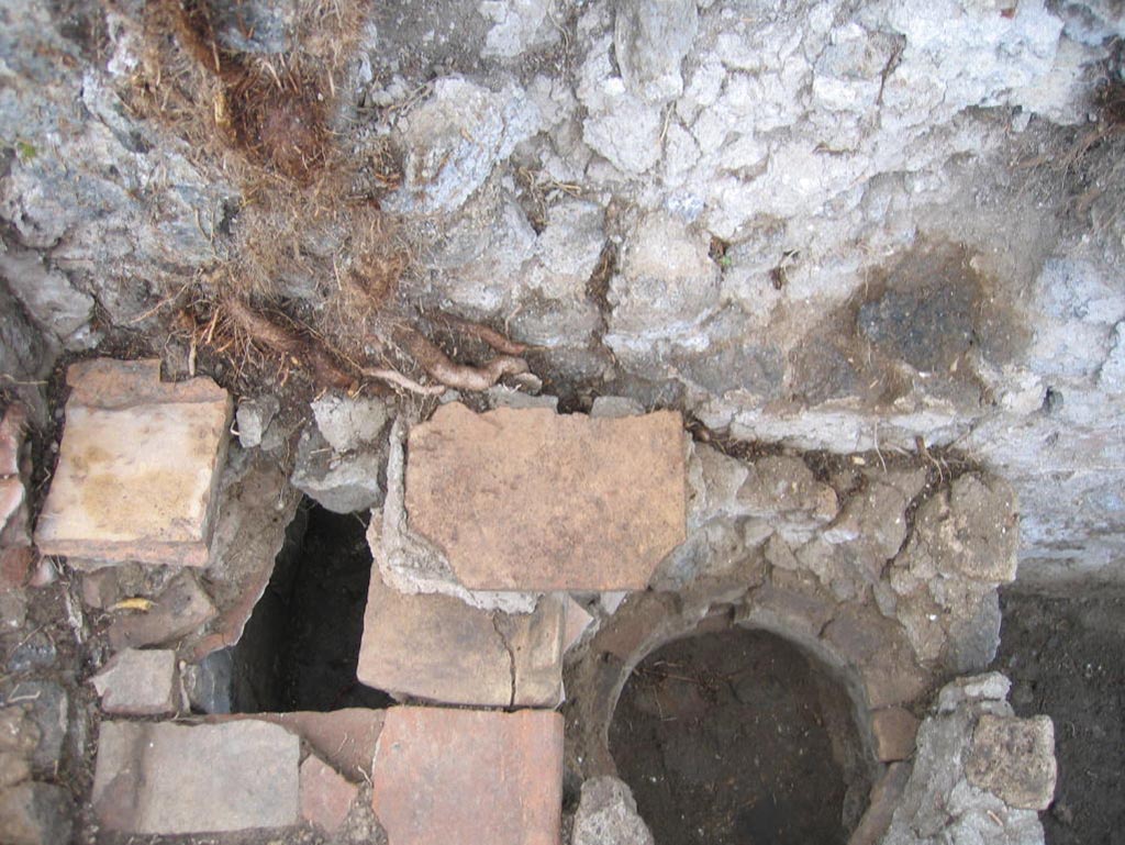 VIII.7.10 Pompeii. August 2005. Looking down onto hearth against south wall in kitchen.
The remains of the niche of the lararium may be still partially visible in the wall above the hearth, upper centre of photo.
Photo courtesy of Pompeii Archaeological Research Project: Porta Stabia.
Site of kitchen, described by Eschebach as having hearth, well and lararium.
See Eschebach, L., 1993. Gebäudeverzeichnis und Stadtplan der antiken Stadt Pompeji. Köln: Böhlau. (p. 389)
According to Boyce, in the wall of the kitchen there was a niche and beside it was a lararium painting.
It represented a sacrificial scene with the Genius and the tibicen, one on each side of an altar.
On either side of them was a Lar. In the lower zone was a single serpent beside an altar.
See Boyce G. K., 1937. Corpus of the Lararia of Pompeii. Rome: MAAR 14. (p.78, no.377).
See Sogliano, A., 1879. Le pitture murali campane scoverte negli anni 1867-79. Napoli: (p.12, no.24, “badly preserved”).
According to Mau -
“Next to the hearth there was the usual painting of the Lares, and a niche.”
See Mau in BdI, 1875, (p.166 - La quarta casa).