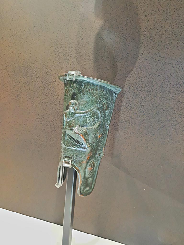 VIII.7.16 Pompeii.
Bronze greave with Aphrodite Euploia (protector of seafarers) sitting on a ship’s prow, inv. 5675. Found 20th December 1766.
Photo taken May 2021, courtesy of Giuseppe Ciaramella.