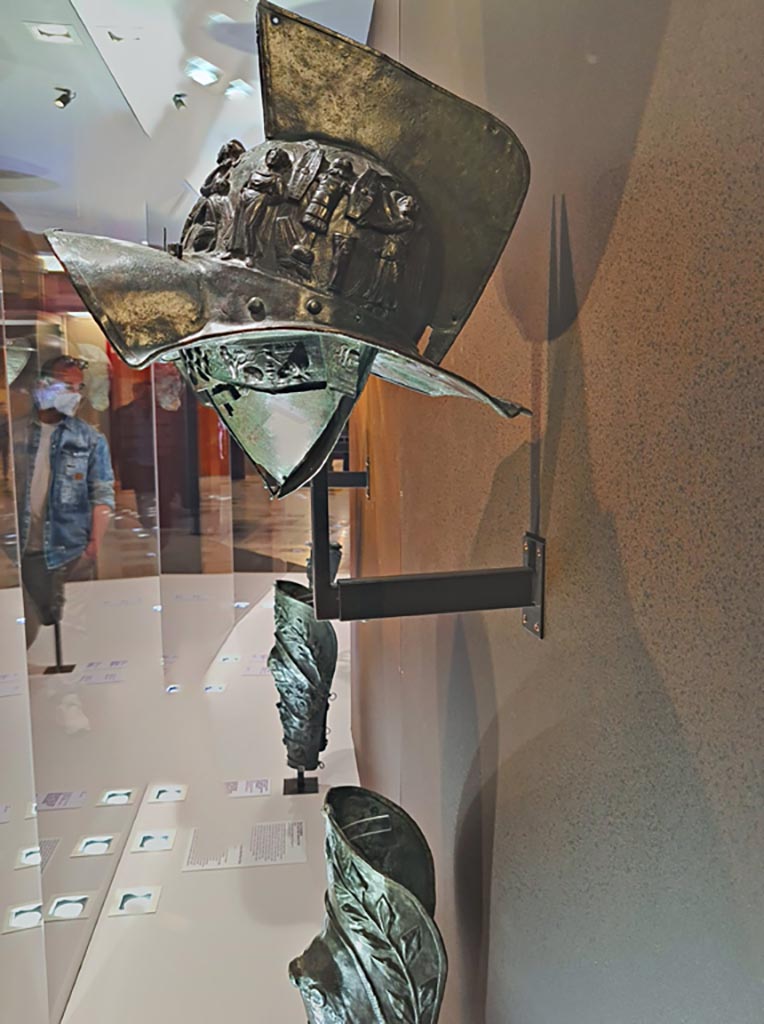 VIII.7.16 Pompeii. Photo taken May 2021, in Naples Archaeological Museum, inv. 5674.
Murmillo gladiator’s helmet, with personification of Rome, Barbarian captives, trophies and Victories, in display case.
Photo courtesy of Giuseppe Ciaramella.