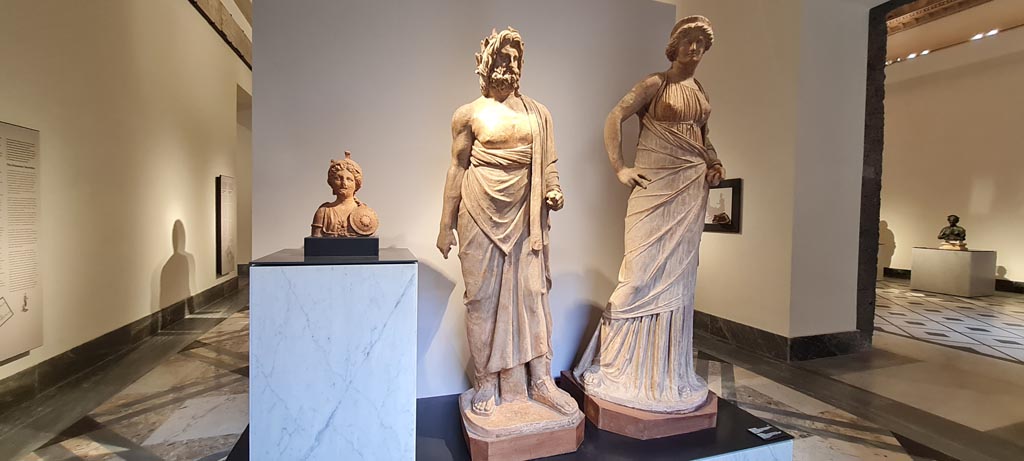 VIII.7.25 Pompeii. April 2023. Three statues found in Temple now said to be of Bellona, Asclepius, and Venus, on display in Naples Museum Campania Romana gallery.
According to the information card in Naples Museum, the two other statues are closely associated with Asclepius. The female statue has been identified as Venus while the bust depicting an armed goddess has been interpreted as Bellona. The deities were cherished by the dictator Sulla and were added when the temple underwent major restoration in about 70 BC.
Photo courtesy of Giuseppe Ciaramella.