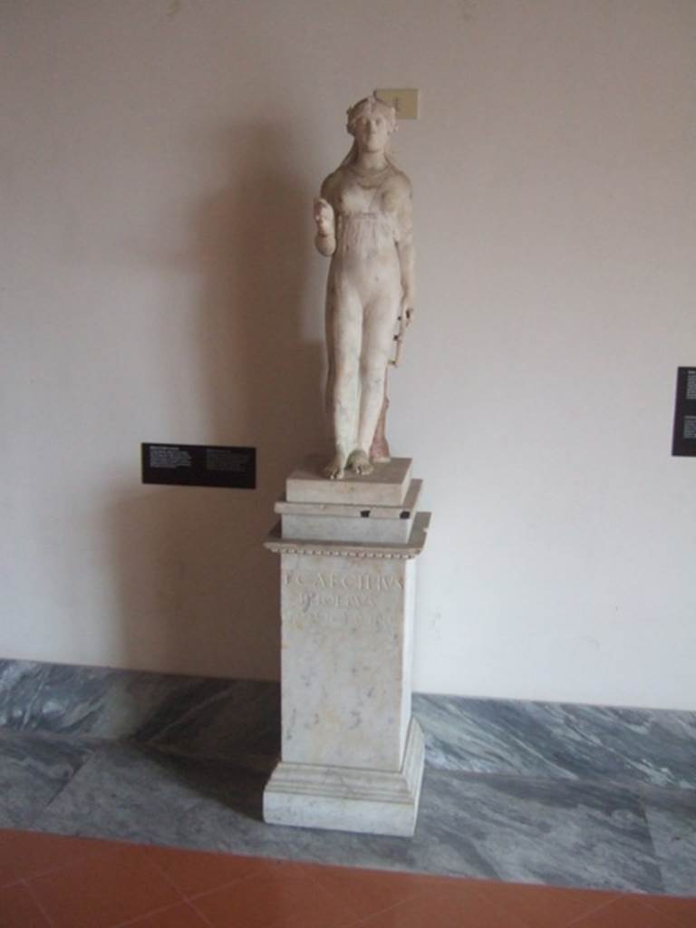 VIII.7.28 Pompeii. Marble statue of Isis holding a sistrum in her right hand (now missing) and key of the Ankh (the key of life or the Nile) in her left.
The key was originally gilded and coloured. The pilaster on which the key leans has the inscription of the freedman L Cecilio Febo. Found in the north east corner of the portico. Now in Naples Archaeological Museum. Inventory number 9976.