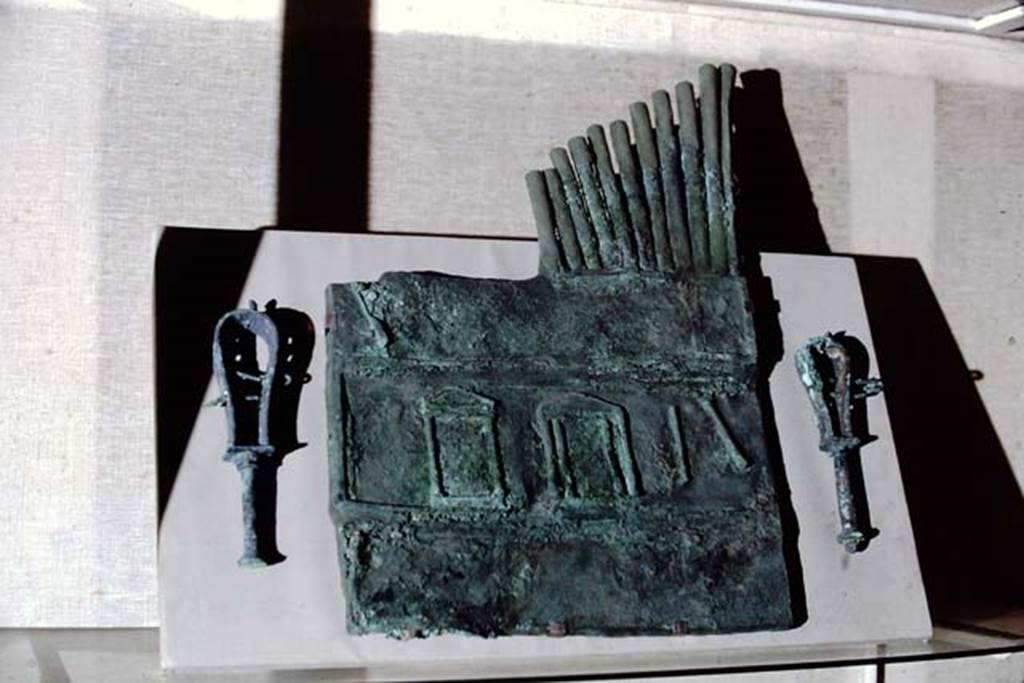 Pompeii, not from this temple. 1968. Pan pipes discovered in 1899. From Villa of Siminius Stephanus.
The Pan pipes are decorated with three aediculae that are supposed to represent a frons scaenae and, at the top, nine rods of different heights.
They are connected at the bottom, and bear a hole near of the mouth.
The object, strongly restored in the nineteenth century, is large, so as to suggest that the operation needed the help of a special machine.
Its use was connected to the satyr play and the myth, but the instruments were also used during ritual ceremonies, such as Isiac processions, during which the faithful waved the sistrum.
It was also used during theatrical performances to entertain banqueters, as music as a separate discipline from acting does not seem to have existed in ancient times.
Now in Naples Archaeological Museum. Inventory number 125187 but shown on the MANN web site as 111055.
Photo by Stanley A. Jashemski.
Source: The Wilhelmina and Stanley A. Jashemski archive in the University of Maryland Library, Special Collections (See collection page) and made available under the Creative Commons Attribution-Non-Commercial License v.4. See Licence and use details.
J68f1410