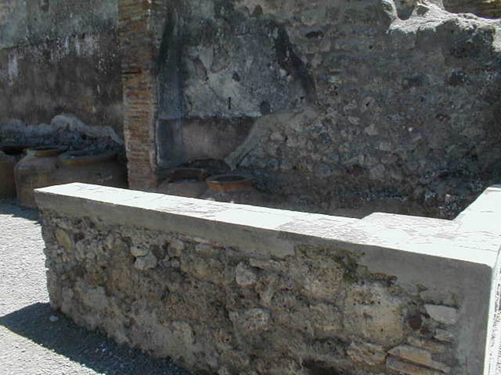 IX.1.3 Pompeii. May 2005. Marble counter. On the south wall of the shop, at the rear of the counter, the remains of the red painted zoccolo and white middle zone of the wall, can be seen.