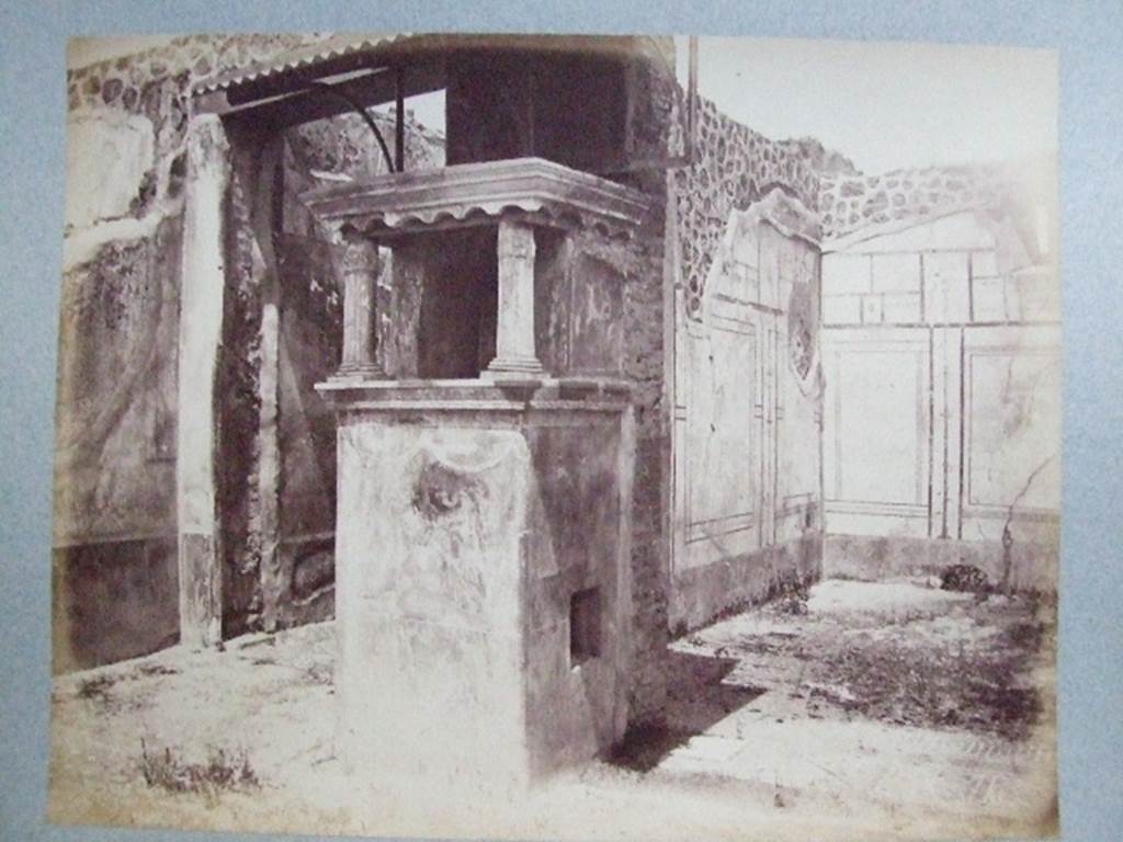 IX.2.26 Pompeii. Lararium situated at south end of east wall of corridor leading to atrium.
Old undated photograph from Fox collection. Courtesy of Society of Antiquaries. According to Bragantini, the triclinium on the east side of the lararium had a floor of cocciopesto, ornamented with a design in white tesserae. It had a border and in the centre had a circle of white tesserae that was the site of the table. The north wall had a small window. The walls were painted with a black dado decorated with painted plants. The middle zone of the walls was white, with panels edged with a border separated by narrow compartments with candelabra. The upper zone was probably white, with architectural paintings.
See Bragantini, de Vos, Badoni, 1986. Pitture e Pavimenti di Pompei, Parte 3. Rome: ICCD. (p.425, triclinio ‘c’).