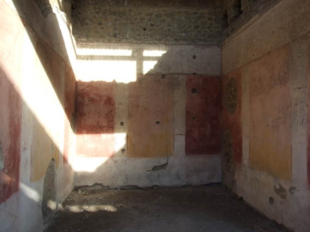 IX.5.11 Pompeii. December 2007. Room 3, looking east. The ala was decorated with red and yellow panels, in half of which were painted Cupids. Under the panels was a black zoccolo, and above them was a frieze finishing above with a stucco cornice. In the small panels of this frieze we see painted on the back (east) wall, a woman’s figure on foot, crowned with fronds and dressed in a green robe, holding a plate or basket in her left hand, and holding the lower edge of her robe with her right hand. On the wall to the right, was a Cupid with club, and under in small rectangles with purple backgrounds, one sees two fighters with daggers. On the wall to the left, finally we have another Cupid, that has in his right hand a bunch of grapes and in the left, an object that cannot be defined, below in a rectangle with purple background, one sees an open volume, on which were painted some black words, in part vanished and difficult to read.
See Notizie degli Scavi, 1877, p.248