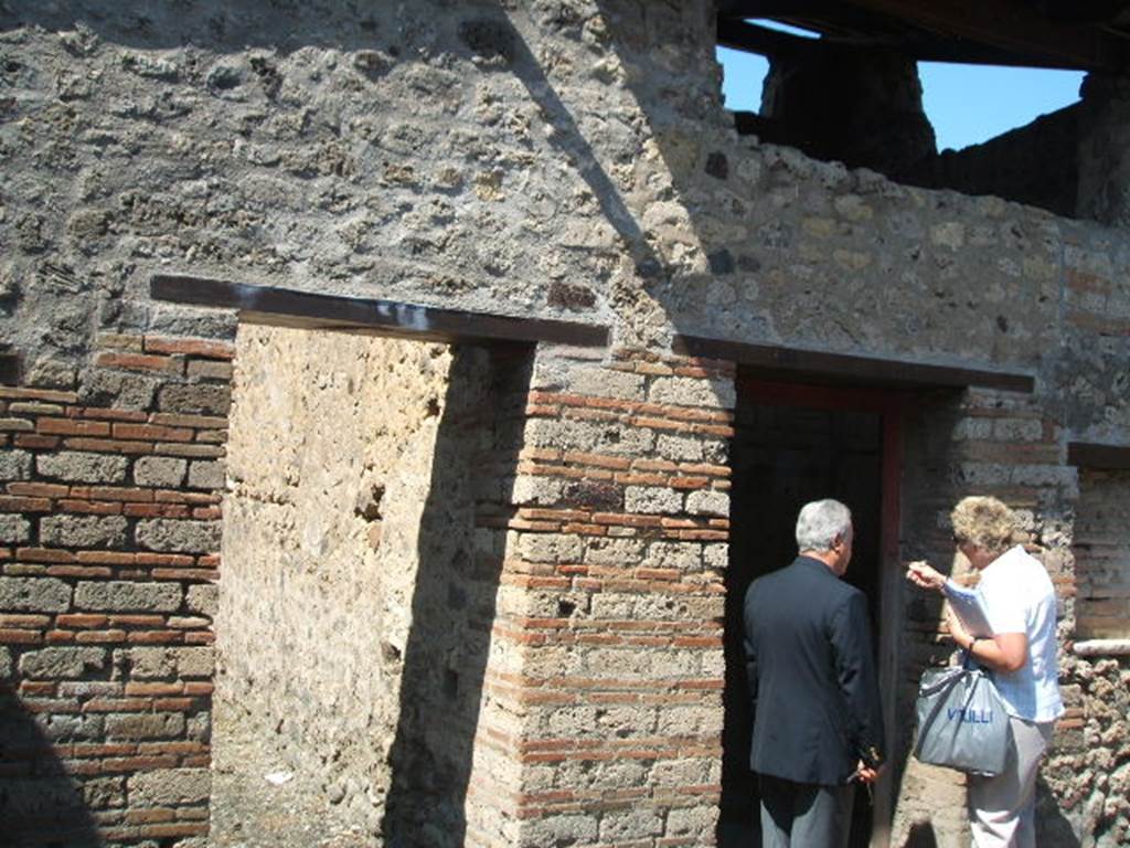 IX.5.16 Pompeii. May 2005. West side of atrium a’, on the left, doorway to kitchen and latrine e’.
On the right, doorway to cubiculum f’.
According to Boyce, on the south wall of the kitchen was a large rectangular panel of white stucco.
On it were painted two yellow serpents with red crest and beards.
These were on either side of a tile embedded and projecting from the wall.
A fire was painted on the wall above the tile.
The background was painted with plants, and across the top were two painted garlands.
On each of the garlands was a painted bird.
See Boyce, G. K., 1937. Corpus of the Lararia of Pompeii. Rome: MAAR 14. (p. 86, no. 425)
In IX.5.16, the first place on the left of the atrium was searched again, and found were several iron nails, some fish bones, and in terracotta: two containers for oil, a vase in fragments, two amphorae, two pot lids, and a broken bowl containing ash.
See Notizie degli Scavi di Antichità, 1885, (pp. 162-4).