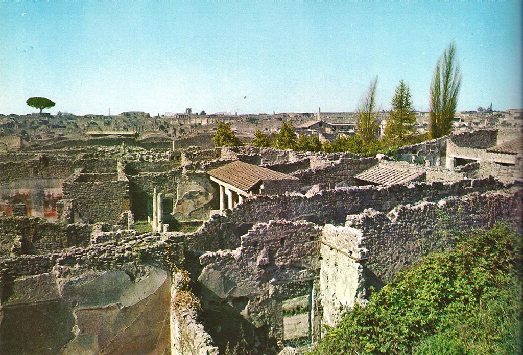 Looking north-west from Casina dell’Aquila to rear of entrance at IX.7.14, lower centre. 1968.
On the left can be seen the west wall of the triclinium of IX.7.12.
The west wall of the garden can be seen behind the greenery, on the right of the doorway.
According to Boyce –
Against the west wall of the garden stands an aedicula, built upon a square masonry base (0.92 square, h.0.70).
The sides of the base are decorated with green plants painted on the white ground.
Above the base, walls enclose a niche (h.0.42, w.0.52, d.0.62).
In front of the structure stands a small altar (0.24 by 0.23, h.0.80).
The roof (no longer preserved) originally extended out over the altar as well as the niche, and the front of it was adorned with a pediment.
It was supported by two columns, the marks of the bases of which are still to be seen near the corners of the base.
On the walls within the niche is the lararium painting.
On the back wall to the right of an altar, stands the Genius pouring a libation upon it.
To the left of the same altar is a serpent, the head of which was done in stucco relief.
On each of the side walls are painted three figures: from back to front – a plant, a Lar, a man in a white garment holding in his left hand an object resembling a black cup, with a patera in his right hand.
He quotes references – Not. Scavi, 1881, 92-93; Bull. Inst., 1883, 146.
In Not. Scavi, it is described as House, only partly excavated – “and corresponds to, after the sixth doorway, west side, counting from the north-west”.
In Bull. Inst, it is described as “West side, first entrance counting from the south, garden in part excavated.”
See Boyce G. K., 1937. Corpus of the Lararia of Pompeii. Rome: MAAR 14. (p.89, no.445).