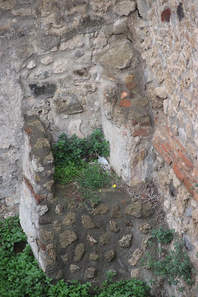IX.7.12, 14 or 16 (?) Pompeii. October 2024.
Garden area “e”, detail of lararium in north-west corner. Photo courtesy of Klaus Heese.
According to Boyce –
Against the west wall of the garden stands an aedicula, built upon a square masonry base (0.92 square, h.0.70).
The sides of the base are decorated with green plants painted on the white ground.
Above the base, walls enclose a niche (h.0.42, w.0.52, d.0.62).
In front of the structure stands a small altar (0.24 by 0.23, h.0.80).
The roof (no longer preserved) originally extended out over the altar as well as the niche, and the front of it was adorned with a pediment.
It was supported by two columns, the marks of the bases of which are still to be seen near the corners of the base.
On the walls within the niche is the lararium painting.
On the back wall to the right of an altar, stands the Genius pouring a libation upon it.
To the left of the same altar is a serpent, the head of which was done in stucco relief.
On each of the side walls are painted three figures: from back to front – a plant, a Lar, a man in a white garment holding in his left hand an object resembling a black cup, with a patera in his right hand.
He quotes references – Not. Scavi, 1881, 92-93; Bull. Inst., 1883, 146.
In Not. Scavi, it is described as House, only partly excavated – “and corresponds to, after the sixth doorway, west side, counting from the north-west”.
In Bull. Inst, it is described as “West side, first entrance counting from the south, garden in part excavated.”
See Boyce G. K., 1937. Corpus of the Lararia of Pompeii. Rome: MAAR 14. (p.89, no.445).