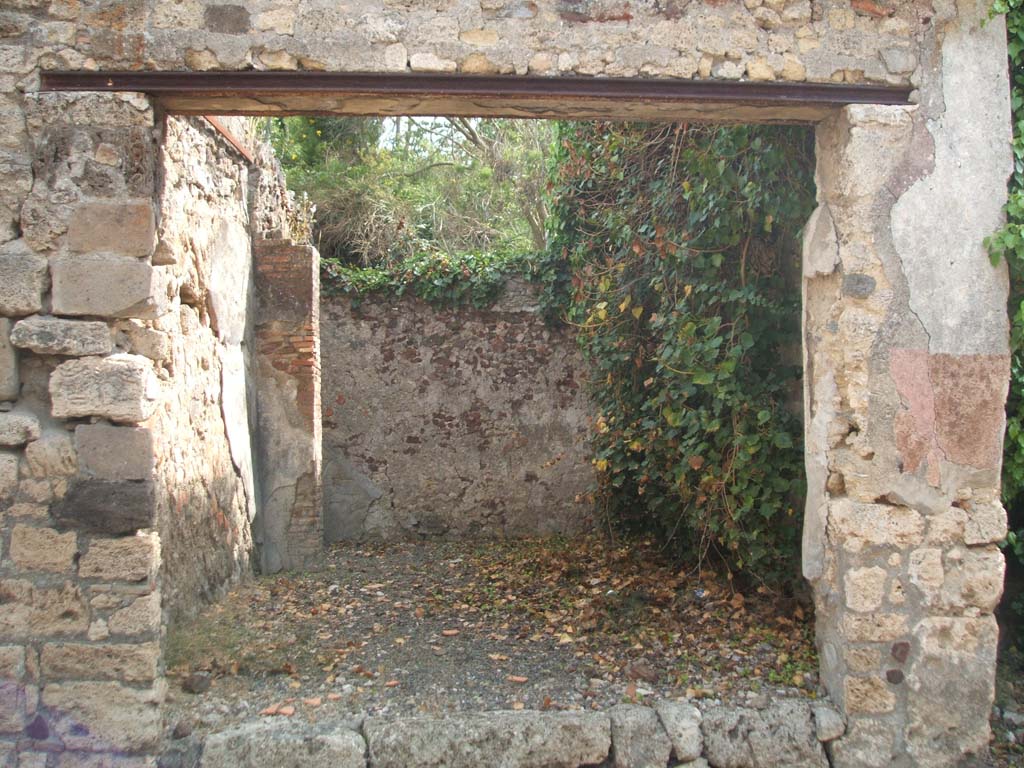 IX.7.18 Pompeii. May 2005. Entrance, looking east across the shop towards the area of a rear room.
According to Mau, the rear room (room e in IX.7.19) was a cubiculum.
He also stated that he thought originally in ancient times the shop, at the front of the photo, would have been closed from the street.
The shop is also described as room “d” in IX.7.19.
The doorsteps of both doorways, IX.7.18 and IX.7.19 were missing when excavated.
It was not known what items were sold in the shop whose walls were covered with white stucco.
Above the entrance, Mau could see a red band which was the remains of a decoration from the 1st style.
See Bullettino dell’Instituto di Corrispondenza Archeologica (DAIR), p.78-9