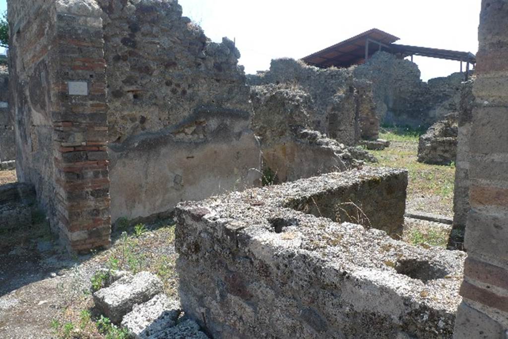 IX.7.22 Pompeii. July 2010. Looking south-east across remains of counter.
Photo courtesy of Michael Binns.
According to Mau, the podium was covered in stucco, red at the front, and rough and reddish at the rear.
The top had been covered with slabs of marble, which were missing.
On the 30th October 1880, six amphorae with inscriptions were found here.
Also found was a broken amphora containing some lentils.
On the 4th February 1881, in the presence of Granduca Nichola di Russia, were found:
• The base of an amphora with unidentifiable burnt material.
• A terracotta lamp
• 3 glass bottles and fragments of a fourth
• Part of the bronze fittings of a chest
• An iron hoe, 11 iron keys and small iron anvil
• 2 bone dies (for game of dice)
• A glass-paste amulet representing a small herm.
See Notizie degli Scavi di Antichità, 1880, p.400, 1881, p. 61-2.
See Mau in BdI, 1882, p. 193.
