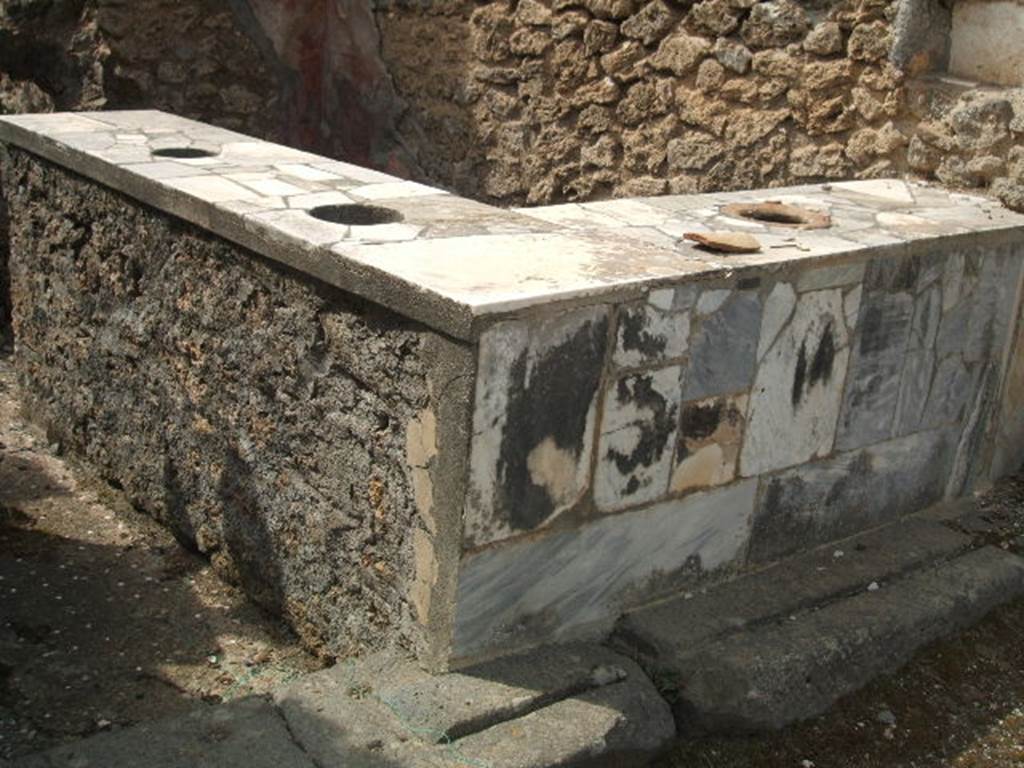 IX.7.24 Pompeii. May 2005.
Marble encrusted two-sided sales counter, inset with three small urns. Looking south-west.
According to Mau, the street door was furnished with a threshold of lava, which closed in the usual manner.
There was also a small door, on the left, to enter by.
The flooring was good opus signinum showing rows of white stones embedded in the crushed brick or tile.
See Mau in BdI, 1882, (p.148)