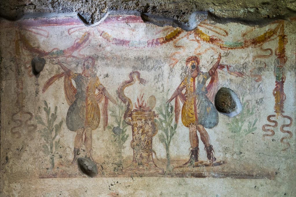 IX.9.c Pompeii. March 2023.
Detail of two Lares either side of a round altar which has a serpent winding around it. Photo courtesy of Johannes Eber.