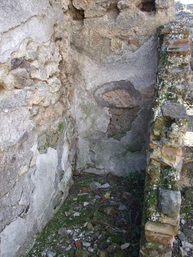 IX.9.e Pompeii. March 2009. Room 16, light yard, south-west corner. Looking west. According to Boyce, in the small open courtyard in the centre of the house, a sacrarium was formed. It was constructed by building a small wall parallel to the south wall, and then covering the enclosure with a sloping roof. At the east end of this enclosure stood a small altar of tufa, originally coated with stucco. The inside surface of the north wall was decorated with a white background and a drawing.
This was of an aedicula and within it a male figure, standing, clad in a yellow tunic. The south wall was also covered with white stucco, the west wall with a coarser variety. A female head of terracotta was found near the sacellum, apparently part of a statue. Not. Scavi, 1889,136; 1891,255. See Boyce G. K., 1937. Corpus of the Lararia of Pompeii. Rome: MAAR 14. (p.92, no.464 )