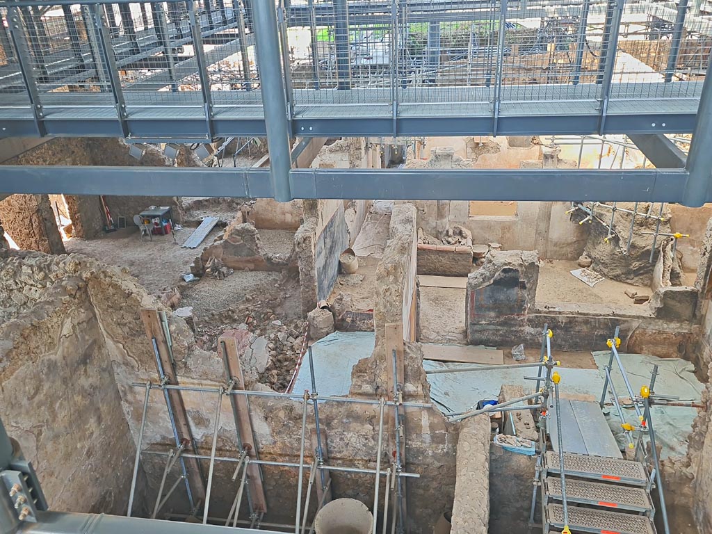 IX.12.4 Pompeii. June 2024. Looking west from above bakery in room “f” of IX.12.6. Photo courtesy of Giuseppe Ciaramella.
The atrium “c” of IX.12.4 is on the left.
On the north side of the atrium are rooms “e” and “f”. Room “f” is at the rear (west) side of the oven, (centre left of above photo).