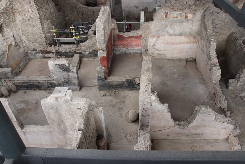 IX.12.4 Pompeii. October 2024.
Looking east towards room “o”, upper left, room “l(L)” with red painted walls, upper centre, and room “f”, on its south side.
On the upper east wall of room “f”, the painting described as from the zoccolo of an upper room, can be seen.
Room “g” can be seen on the extreme right, with doorway into atrium “c”. Photo courtesy of Klaus Heese.