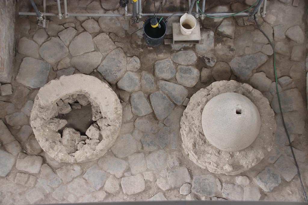 IX.12.6 Pompeii. October 2024. Bakery room “f”, two mill bases between oven “d” and north wall.
Photo courtesy of Klaus Heese.