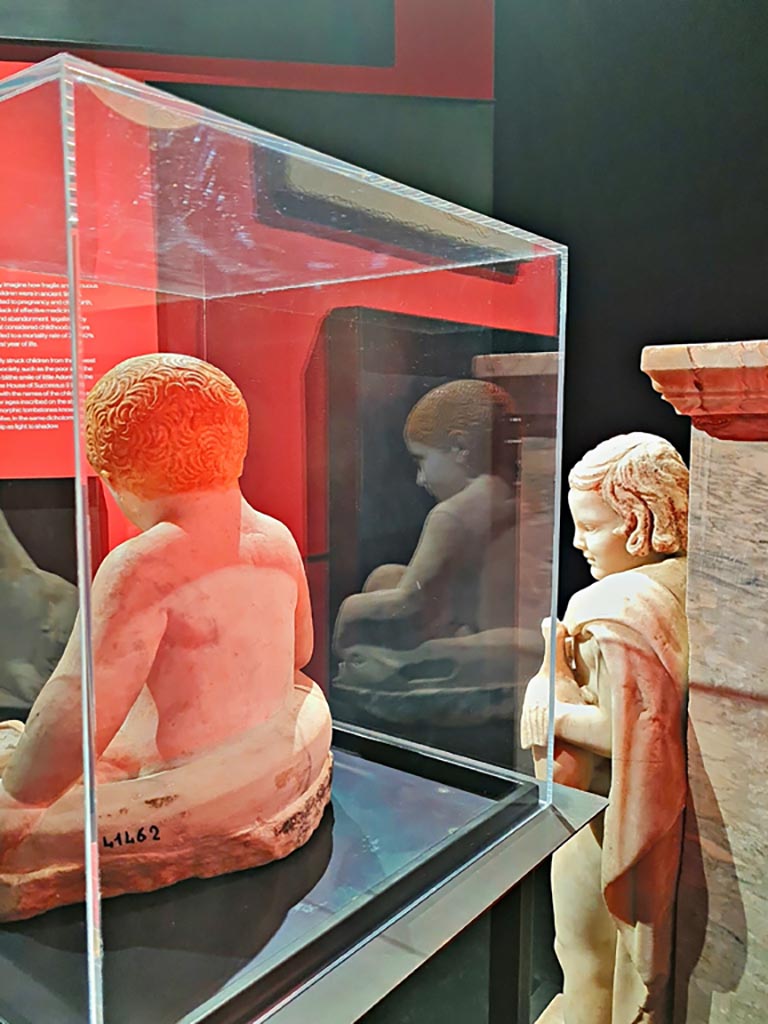 IX.12.9 Pompeii. March 2024. Fountain statuette of a boy and dolphin. Marble 1st century AD.
(Statuetta di fontana con bambino e delfino. Marmo, l sec. D.C.)
Provenanced from this house according to the information card at the exhibition entitled -
“L’altra Pompei, vite comuni all’ombra del Vesuvio”. Photo courtesy of Giuseppe Ciaramella.
According to an information card in the house –
“The garden was also decorated with a fountain which was crowned with a statue of a young boy, on which we can identify traces of original colours.”