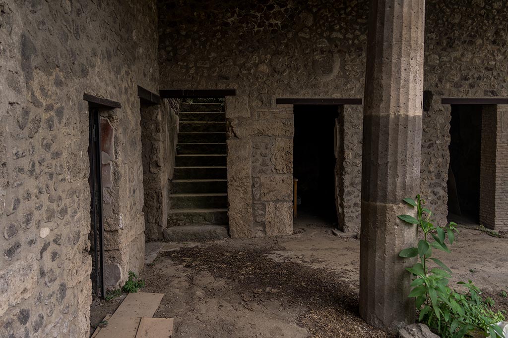 IX.14.4 Pompeii. July 2024.
Looking west in south-west corner of peristyle with steps to upper floor, and room 12, in centre. Photo courtesy of Johannes Eber.
