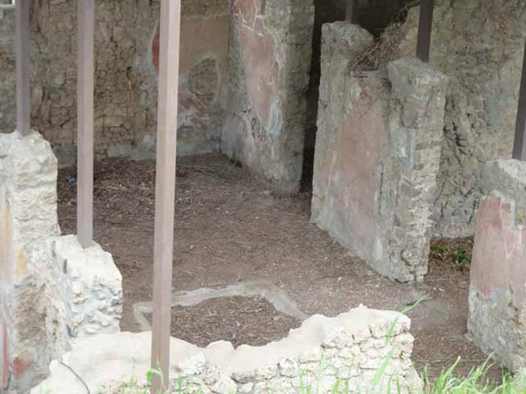 IX.14.c Pompeii. May 2010. Looking north across atrium 2 with impluvium (a), which was square consisted of a simple groove in the floor. At the north end of the impluvium was a masonry feature, yellow on the outside, semi-circular inside. There was a hole in the centre from which water flowed into the impluvium. The atrium floor and that of the fauces were of opus signinum. On the west side of the Tuscan atrium was a cistern mouth (b) made of lava stone. There are two doors in rear (east) wall. The narrower doorway is the entrance to room 6. The wider (nearer) doorway is to the small portico 9 and this leads to the garden 3 and kitchen and latrine 11.
