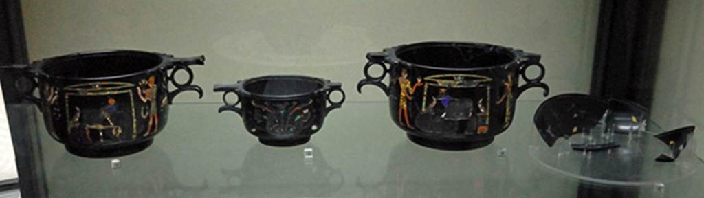 Villa San Marco, Stabiae. Found in room 37, May 1954, near the south east wall.
Three obsidian Skyphii (cups) with Egyptian scenes inlaid in gold and mosaic and fragments of a phiale (broad flat container) with Nilotic scenes.
From left to right they are Skyphos A, C, B and the phiale.
Photographed December 2007 in Naples Archaeological Museum. Inventory numbers 294471, 294472, 294473 and 294474.
See Barbet A. (a cura di), 1999. La Villa San Marco di Stabia: Illustrazioni 1. Roma, L’Erma di Bretschneider. Figs. 717 to 723.
See Elia O., 1957. Le coppe ialine di Stabia, in BdA, 42. pp. 97-103.