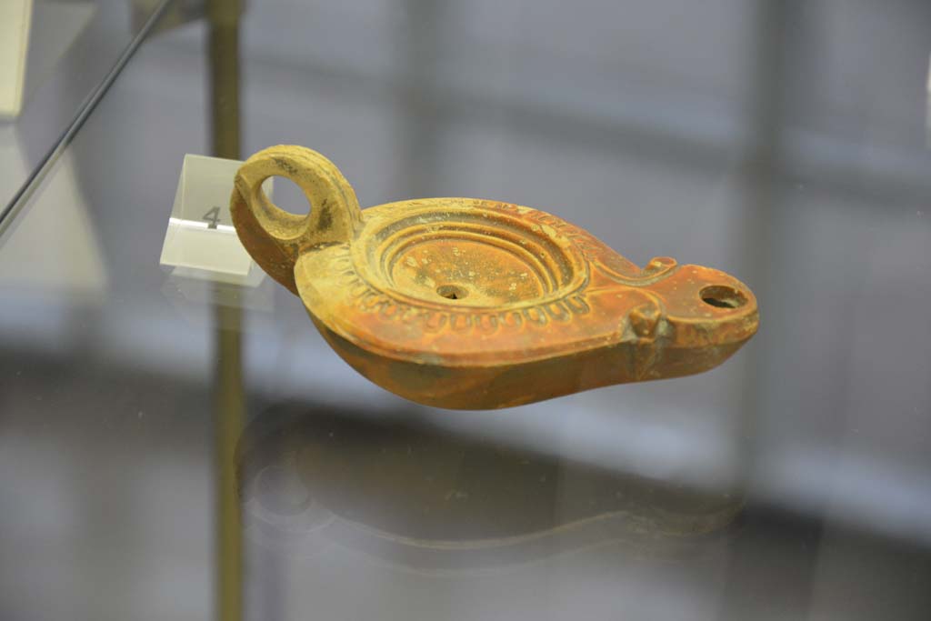 Villa Regina, Boscoreale. April 2017. Above, no.4, terracotta one-handled single flame lamp. Photo courtesy of Adrian Hielscher.
Villa Regina, Boscoreale, (from information card) –
The terracotta lamps found in the villa are of a one handled type, with a beak from which the flame shone. On the bronze support would have leaned the lamp.
A lamp, which bears a cross sign on the external base, documents the human presence in the area of the villa after the eruption of 79AD.
Le Lucerne fittili rinvenuti nella villa sono di tipo monolicne, ad un becco da cui fuoriusciva la fiamma. Sul sostegno di bronzo veniva poggiata la lucerna.
Una lucerna, che reca sul fondo esterno un segno a croce, documenta la presenza umana nell’area della villa dopo l’eruzione del 79AD.
No.3 (not photographed). A bronze support for a lamp, found in room 2, dateable from Ist century AD.
Nos. 4-6. One-handled lamps, made of terracotta, dateable from 1st century AD.
No.7 (not photographed). A one-handled lamp, made of terracotta, dateable from II to IV century AD.
