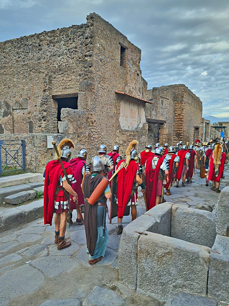 Via dell’Abbondanza, north side. 28th September 2024. Roman Legionary re-enactors marching.
Looking north-east towards III.2.1, on left, towards III.2.2 and III.2.3, on right, during “Ludi Pompeiani” event.
Photo courtesy of Giuseppe Ciaramella.