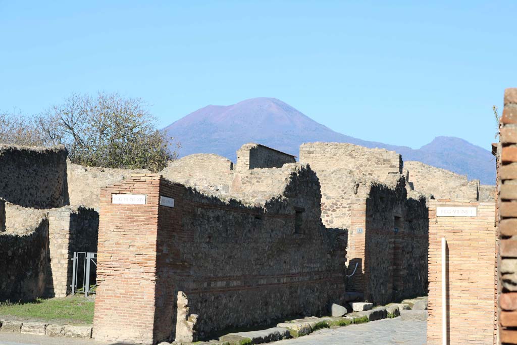 Via dell’Abbondanza, north side at VII.14.14, Pompeii, on left. December 2018.
Looking north-west at junction with Vicolo del Lupanare, with Vesuvius towering above. Photo courtesy of Aude Durand.
