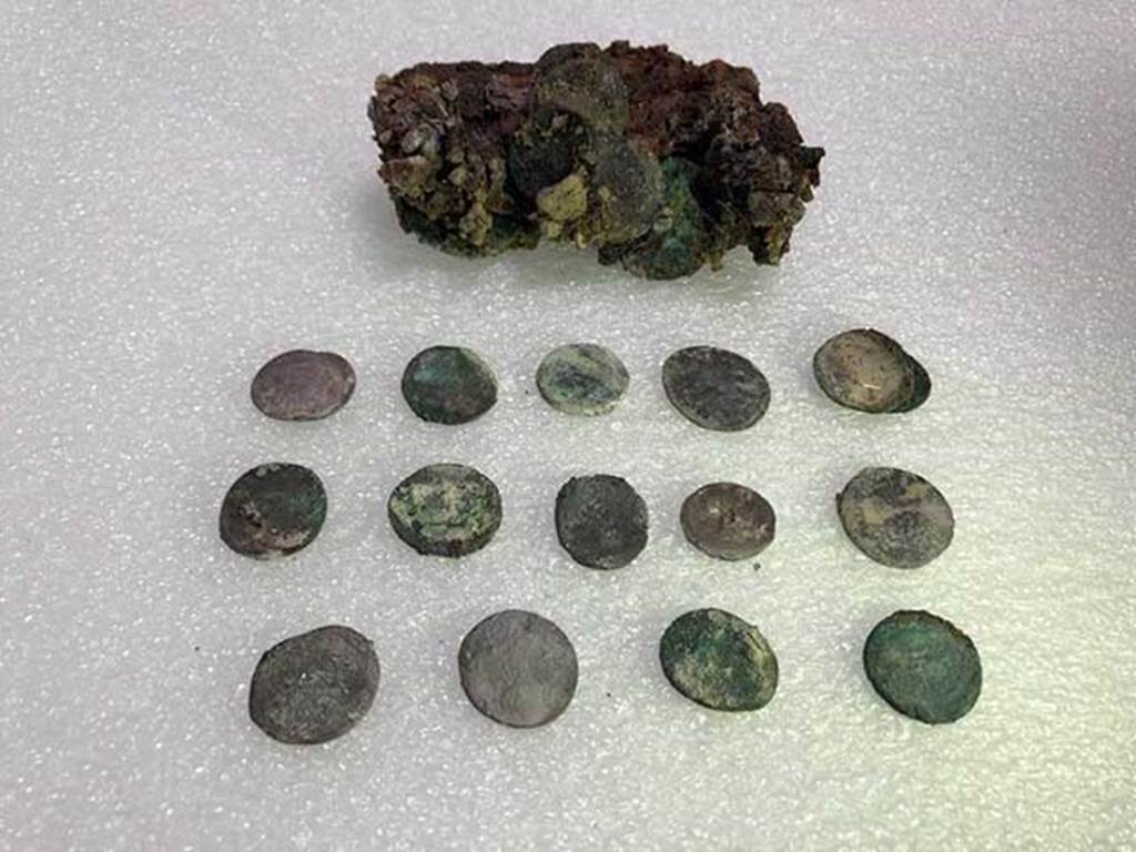 Vicolo delle Nozze d’Argento with the Vicolo dei Balconi intersection. Leather pouch containing coins found under Pompeii skeleton.
At first examination there would seem to be at least 20 silver denarii and two bronze asses with a nominal value of eighty sesterces and a half.
Such a quantity of coins could at that time guarantee the maintenance of a family of three for 14 to 16 days.
The coins have a very varied chronology. It was possible to examine 15 coins, for the most Republican, starting from mid-2nd century BC.
One of the later Republican coins, is a Legionary Denarius of Mark Antony, common in Pompeii, with the indication of the XXI legion.
Among the few identified imperial coins, a probable denarius of Octavian Augustus and two denarii of Vespasian.
Photograph © Parco Archeologico di Pompei.