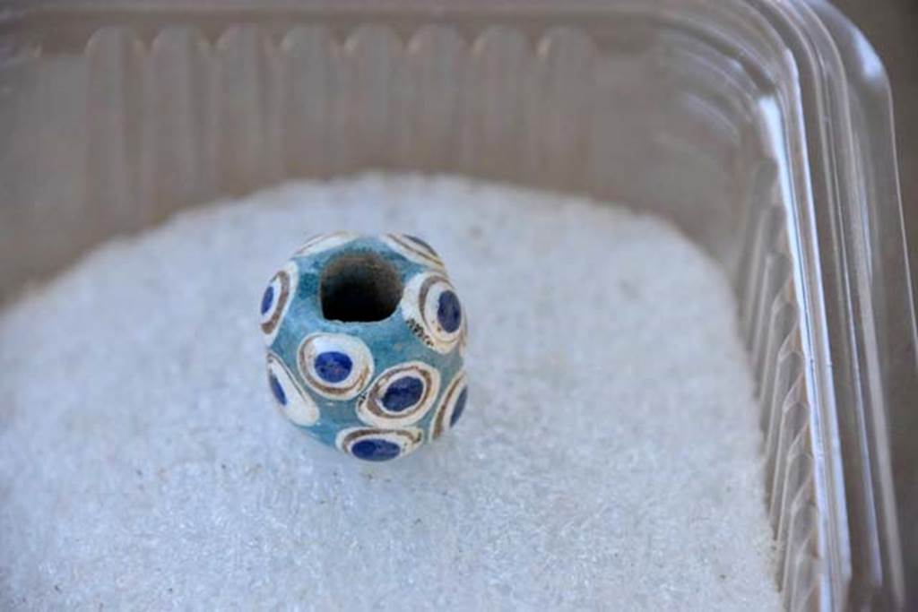 Santuario extraurbano del Fondo Iozzino. 2014 excavations. A turquoise bead decorated with gold, white and blue ringed patterns.
Una perla turchese decorata con motivi ad anello oro, bianco e blu.
Photograph © Parco Archeologico di Pompei.