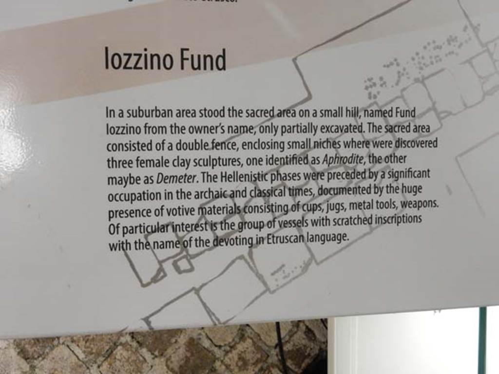 Santuario extraurbano del Fondo Iozzino. May 2018. Information card in exhibition.
The sacred area consisted of a double fence, enclosing small niches where were discovered three female clay sculptures, one identified as Aphrodite, another maybe as Demeter.
The Hellenistic phases were preceded by a significant occupation in the archaic and classical times, documented by the huge presence of votive materials, consisting of cups, jugs, metal tools and weapons.
Of particular interest is the group of vessels with scratched inscriptions with the name of the devotees in Etruscan language.