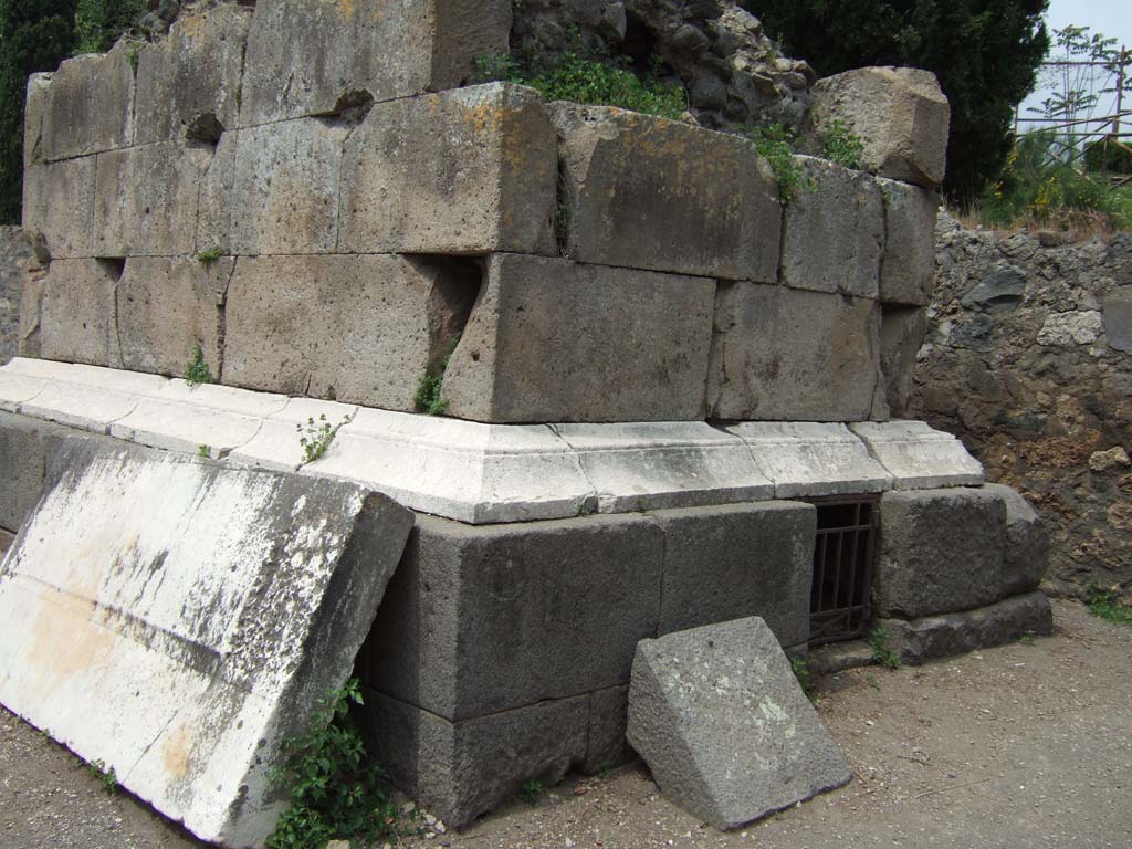 HGE01 Pompeii. May 2006. West side, and south side with doorway to grave chamber.
In 1887 Sogliano opened the grave chamber and found, covered in earth, two cremation urns enclosed in lead containers.
Between the bones in the urns was an As of Cn. Piso (c. 23BC), and an As of P. Lurius Agrippa (c. 7BC).
Also found were the remains of wood work and nails, parts of one of more small boxes richly decorated in ivory, and a broken small clay ointment bottle.
See Kockel V., 1983. Die Grabbauten vor dem Herkulaner Tor in Pompeji. Mainz: von Zabern. (p.111-5, Taf. 32-33).
According to Garcia y Garcia, a bomb fell near here in September 1943.
This caused the partial destruction and shattering of some blocks of the footings on the east side of this tomb, which had not yet been finished in 79AD.
See Garcia y Garcia, L., 2006. Danni di guerra a Pompei. Rome: L’Erma di Bretschneider. (p.160)