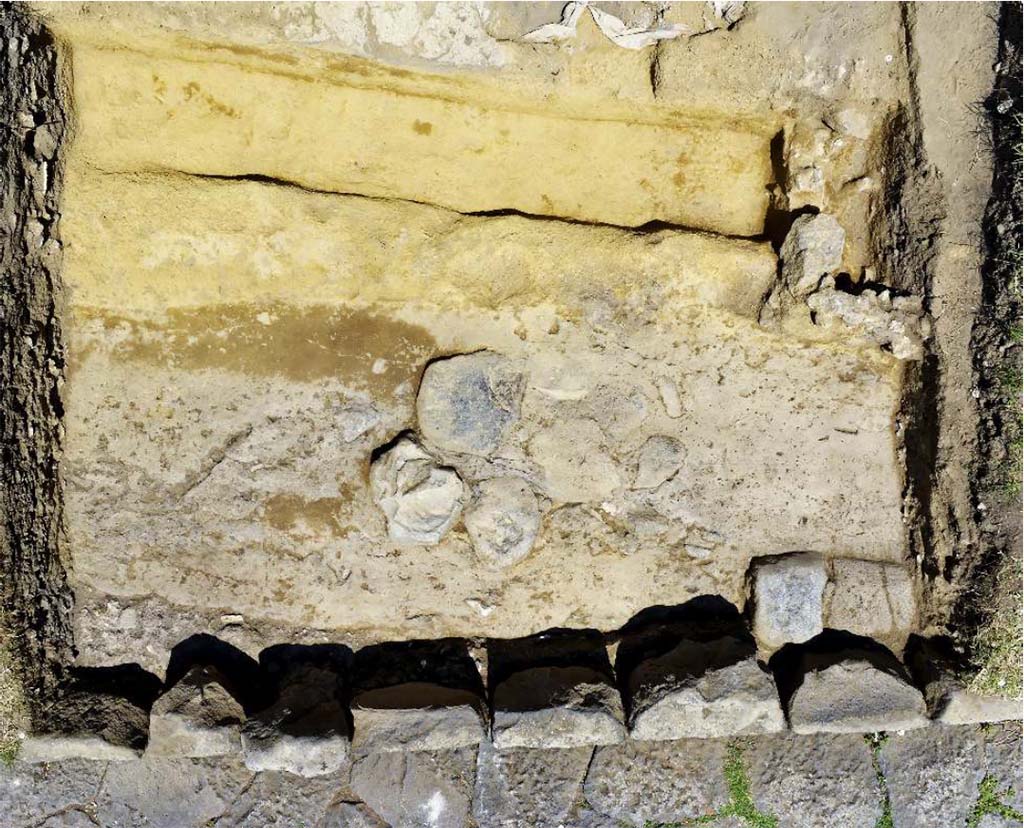 Fig. 10 – Zenithal view of the paved road intercepted between the portico and via dei Sepolcri in front of the N20a fountain.
Photo: B. Lemaire-EFR.
In front of the fountain, a paved path whose axis diverges appreciably from the current via dei Sepolcri, was found about 0.40 m below the level of the embankment which, from the current path, rises slightly to the level circulation of the gantry (fig. 10). It is quite probable that this road, whose pavement clearly bears the marks of recharging and repairs, is to be related to a segment of paved road discovered a few metres further upstream, in front of the HGE14 shop (fig. 11). The two segments are paved with basalt slabs of dimensions appreciably smaller than those of the way in use in 79.
Fig. 10 – Vue zénithale de la voie dallée interceptée entre le portique et la via dei Sepolcri devant la fontaine N20a.
Cliché : B. Lemaire-EFR.
Devant la fontaine, une voie dallée dont l’axe diverge sensiblement de l’actuelle via dei Sepolcri, a été retrouvée à environ 0,40 m sous le niveau du talus qui, depuis la voie actuelle, monte en légère pente jusqu’au niveau de circulation du portique (fig. 10). Il est assez probable que cette voie, dont la chaussée porte clairement des marques de recharges et de réfections, soit à mettre en relation avec un segment de voie dallée découvert quelques mètres plus en amont, devant la boutique HGE14 (fig. 11). Les deux segments sont pavés avec des dalles de basalte de dimensions sensiblement inférieures à celles de la voie en usage en 79.
See Pompéi, Porta Ercolano : organisation, gestion et transformations d’une zone suburbaine : Campagne 2016. CEFR 1676