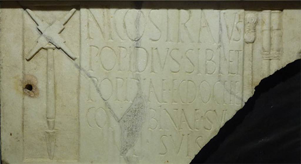 Pompeii Porta Nocera Tomb 17aOS. Found on 13th December 1956. 
Marble relief from the tomb of Popidius Nicostratus with inscription
NICOSTRATVS
POPIDIVS SIBI ET
POPIDIAE ECDOCHE
CONCVBINAE SVAE 
ET SVIS
Photo courtesy of Michael Binns. SAP inventory 11737.

The inscription reads

Nicostratus
Popidius sibi et
Popidiae Ecdoche
Concubinae suae 
et suis

According to Cooley this translates as 
Nicostratus Popidius (erected this monument) for himself and his concubine Popidiae Ecdoche and his family.
See Cooley, A. and M.G.L., 2004. Pompeii : A Sourcebook. London : Routledge. H60b, p. 178.

According to D’Ambrosio, the relief was found in pieces, reused in the floor and vault of the tomb.
It was not therefore related to the tomb.
It represents the tools of a surveyor.
On the left is a representation of a groma. 
On the right is a length of coiled cord and two measuring rods tied together. 
In the incomplete corner was probably a lead plumb line (perpendiculum), which was used with the groma.
See D’Ambrosio, A. and De Caro, S., 1983. Un Impegno per Pompei: Fotopiano e documentazione della Necropoli di Porta Nocera. Milano: Touring Club Italiano. 17a b OS.

According to Sampaolo, the epigrafic characters and the tablets reuse indicate Popidius Nicostratus was probably active in the first decades of the first century d.C./A.D.
Perhaps the grave of Nicostrato, damaged by the 62 earthquake, was not restored anymore.
See Sampaolo V., in Pompei 1748-1980, I tempi della documentazione. p. 206-7.
