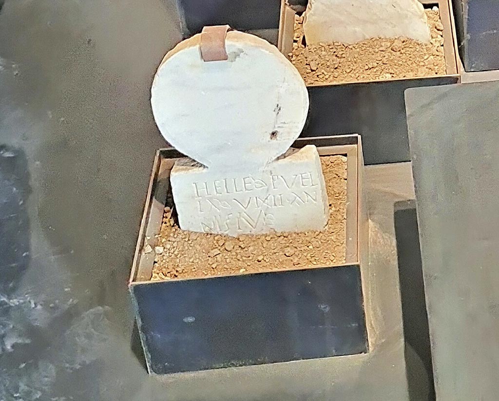 Pompeii Porta Nocera. Tomb 19aOS. Cippus of Helle Puella.
On display in exhibition “L’altra Pompei, vite comuni all’ombra del Vesuvio”.
Photo courtesy of Giuseppe Ciaramella.
A marble columella was found with the inscription -

HELLE PVEL
LA VIXIT AN
NIS IV.

This reads as 

Helle Puella vixit annis IV

The tomb name is unknown, and according to De Caro, it is unlikely to be that of the four-year-old slave Helle Puella.
See D’Ambrosio, A. and De Caro, S., 1983. Un Impegno per Pompei: Fotopiano e documentazione della Necropoli di Porta Nocera. Milano: Touring Club Italiano. (19aOS).
