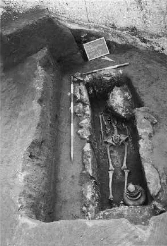 Pompeii Porta Sarno Necropolis. 1999.
Skeleton in inhumation tomb from the Samnite period, encased in travertine blocks.
The first tomb explored contained a single skeleton with the head to the west. At the feet were the grave goods, consisting of an achromatic olla, a black varnished kylix, stamped with 6 rosettes joined by circular arcs, a black varnished oinochoe, with a round mouth. They are, as can be seen, poor burials dating back to between the mid-4th and the beginning of the 3rd century a. C.
Scheletro in tomba ad inumazione di età sannitica, a cassa di blocchi di travertino.
La prima tomba esplorata conteneva un solo scheletro con testa ad ovest. Presso i piedi era il corredo, costituito da un'olla acroma, una kylix a vernice nera, con stampigliatura a 6 rosette congiunte da archi di cerchio, una oinochoe a vernice nera, con bocca rotonda. Sono, come si vede, sepolture povere databili tra la metà del IV e gli inizi del sec. III a. C.
See/Vedi Suburbio Orientale in Rivista di Studi Pompeiani X, 1999, p. 180, fig. 1.