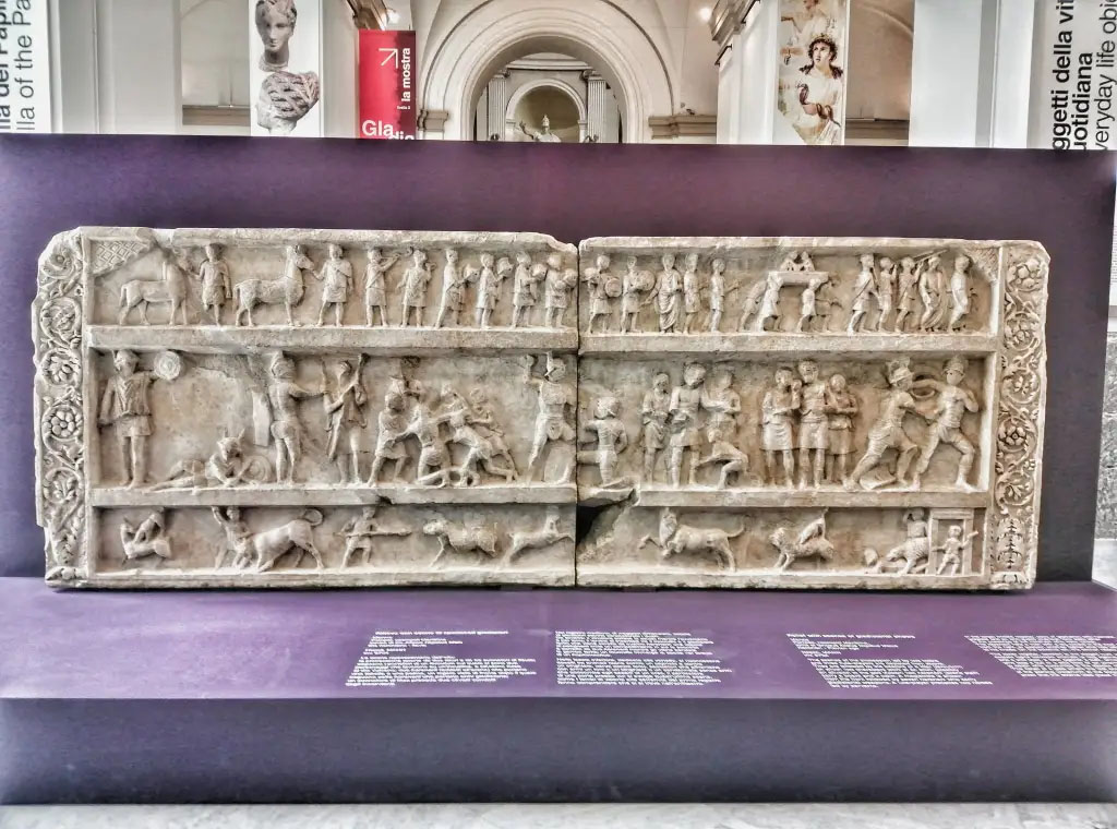 SG6 Pompeii. 2021. Gladiatorial relief with hunting scenes from a tomb at Porta Stabia. The background gives an indication of its large size.
According to Emmerson, this relief measures more than 4 metres long and 1.5 metres high.
See Emmerson A., 2010. Reconstructing the Funerary Landscape at Pompeii's Porta Stabia: Rivista di Studi Pompeiani 21, pp. 78, fig. 1.
According to Osanna, in view of what remains and the visible traces, as well as archive research that is still ongoing, it is more than likely that the top of the tomb SG6, damaged by the construction of the San Paolino building in the nineteenth century, was completed with the gladiator relief preserved in MANN. If you evaluate the role that gladiatorial shows and venations have in praise, it can be assumed that the well-known relief with gladiatorial scenes and hunts with animals kept in Mann was placed there.
The relief has dimensions compatible with the monument SG6, as its length is about 4 metres long, and would respond well in the theme to the role of the deceased as an extraordinary organizer of games.
Moreover, the relief, discovered by the superintendent Avellino in the 1840s, was found out of place (from the damage evidently suffered by the monument in the construction of San Paolino), precisely in the area of Porta Stabia.
Now in Naples archaeological Museum. Inventory number 6704.
SG6 Pompeii. 2021. Rilievo gladiatore con scene di caccia da una tomba a Porta Stabia. Lo sfondo dà un'indicazione delle sue grandi dimensioni.
Secondo Emmerson, questo rilievo misura oltre 4 metri di lunghezza e 1,5 metri di altezza.
Vedi Emmerson A., 2010. Reconstructing the Funerary Landscape at Pompeii's Porta Stabia: Rivista di Studi Pompeiani 21, pp. 78, fig. 1.
Secondo Osanna, in considerazione di quanto resta e delle tracce visibili, oltre che delle ricerche di archivio tuttora in corso, è più che verosimile che la parte superiore della tomba SG6, danneggiata dalla costruzione dell’edificio di San Paolino nell’Ottocento, fosse completata con un rilievo conservato al MANN. Se si valuta il ruolo che gli spettacoli gladiatori e le venationes hanno nell’elogio, si può ipotizzare che fosse ivi collocato il noto rilievo con scene gladiatorie e di caccie con animali conservato al Mann.
Il rilievo ha infatti dimensioni compatibili con il monumento SG6, lungo com’è circa 4 m., e risponderebbe bene nel tema al ruolo del defunto di straordinario organizzatore di giochi.
Inoltre, il rilievo, scoperto dal soprintendente Avellino negli anni ’40 del XIX secolo, fu rinvenuto fuori posto (per i danni subiti dal monumento evidentemente per la costruzione di san Paolino), proprio nell’area di porta Stabia.
Ora al Museo archeologico di Napoli. Numero di inventario 6704.