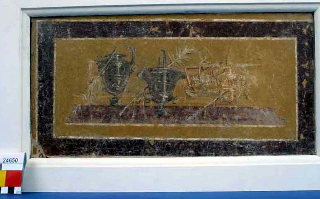 Villa della Pisanella, Boscoreale. Fresco fragment. Decorative compartment with representation of three vases with palm tree branches.
According to De Cou, the first vase has a wide lip and short neck and is painted to represent a metal surface with raised rings. On the left side of the lower part of the body there is a ring handle with ornamental attachment, a projecting head like that of a horse, and on the stem a festoon of ribbon.
The second vase has flaring sides and a high base and is also painted to represent a metal surface with raised rings.
The third vase, standing some distance to the right, is shaped like the first but only drawn in outline with raised bands in the centre like the others.
Between the second and third vases is a mat on which is a table with three straight legs visible and an object on top.
At the right hand end is another table on which an object resembling a cup with a handle is sketched.
See De Cou F. Antiquities from Boscoreale in Field Museum Of Natural History (January 1, 1912), p. 166-7.
Photo © Field Museum of Natural History - CC BY-NC.
Now in the Field Museum, inventory number 24650. See in Field Museum