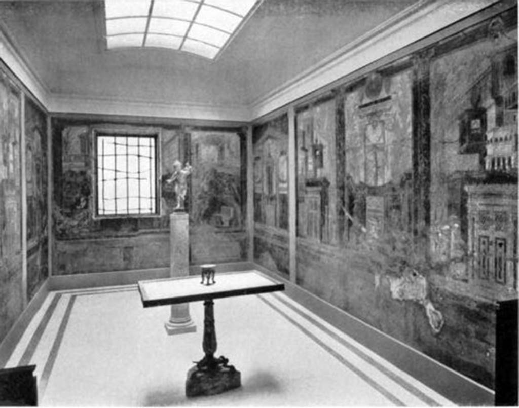 Villa of P. Fannius Synistor at Boscoreale. Cubiculum M and alcove, 1910. As displayed with frescoes and mosaic floor after the relocation of the room within the gallery. The new arrangement introduced light through the window and from a skylight in the ceiling. Note the plain mosaic floor. The table in the centre and the bronze figure “Running Eros, Holding a Torch” are said to be from “a villa in Boscoreale”. The bronze figure “Running Eros, Holding a Torch” is now in the Pierpoint Morgan Library in New York City. The marble table had a bronze rim decorated with a beautiful design inlaid with silver and niello. It was found in pieces and was put together with some restorations, especially in the leg.