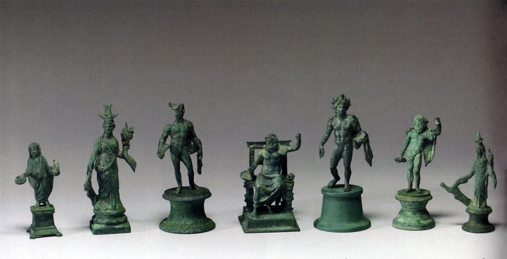 Boscoreale, La villa del Fondo Acunzo. 1903. Room 12. Podium “y”.
Group of seven bronze statuettes found on podium built against the east wall of the room which opened off the kitchen 8.
Left to right: Genius familiaris, large Isis Fortuna, Mercury, seated Jupiter, Helios, standing Jupiter, small Isis Fortuna.
Now in The Walters Art Museum, Baltimore.