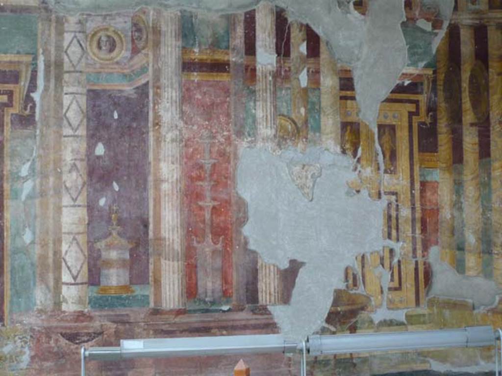 Oplontis, May 2010. Room 5, detail from centre of west wall. Photo courtesy of Buzz Ferebee. On each wall are two painted large false doors, all painted with a figure of a victory on the doors, and landscape painted panels above the door lintels, There are also shields with portrait heads between flanking columns to appear rich in quality.