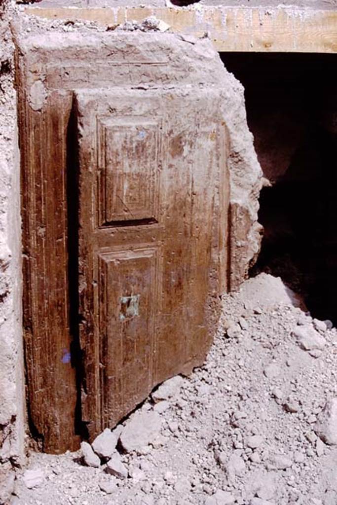 Oplontis Villa of Poppea, 1975. Cast of original wooden door emerging from lapilli. Photo by Stanley A. Jashemski.
Source: The Wilhelmina and Stanley A. Jashemski archive in the University of Maryland Library, Special Collections (See collection page) and made available under the Creative Commons Attribution-Non Commercial License v.4. See Licence and use details.
J75f0141
According to the Parco Archeologico di Pompei, the excavations have offered the opportunity to learn more about the functions and structure of the service galleries connecting various parts and terraces of the Villa. During the excavations in one of the galleries, a cast of the lower left half of the wooden access door was made. The original door had been decorated in pale blue colours before being completely destroyed and burnt. Initially it had been launched into the corridor due to the force exerted by the accretionary lapilli, and then preserved thanks to the solidification of a layer of Volcanic ash typical of pyroclastic flows.
See https://pompeiisites.org/en/excavations-plan-en/villa-a-of-oplontis/