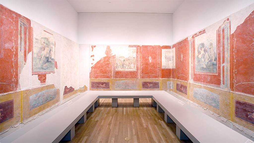 Gragnano, Villa rustica in Località Carmiano, Villa A. Triclinium 1.
Reconstruction of room, looking south.
The three walls had each a central panel with a fresco and side panels with female figures in flight.
Architectonic perspectives which continued round the corners, suggested a unitary space removing the corners and giving continuity to the walls.
See Bonifacio G., 2004. In Stabiano: Exploring the Ancient Seaside Villas of the Roman Elite. Castellamare: Nicola Longobardi, p. 72.